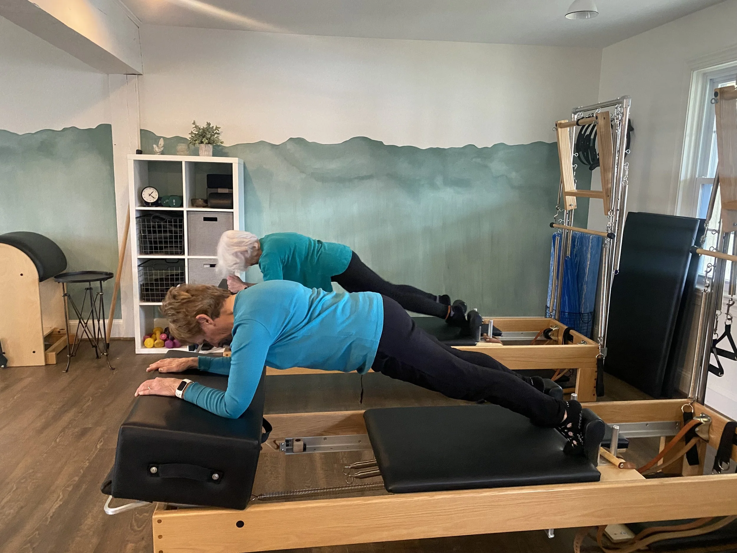 Two participants practicing together on Pilates reformers